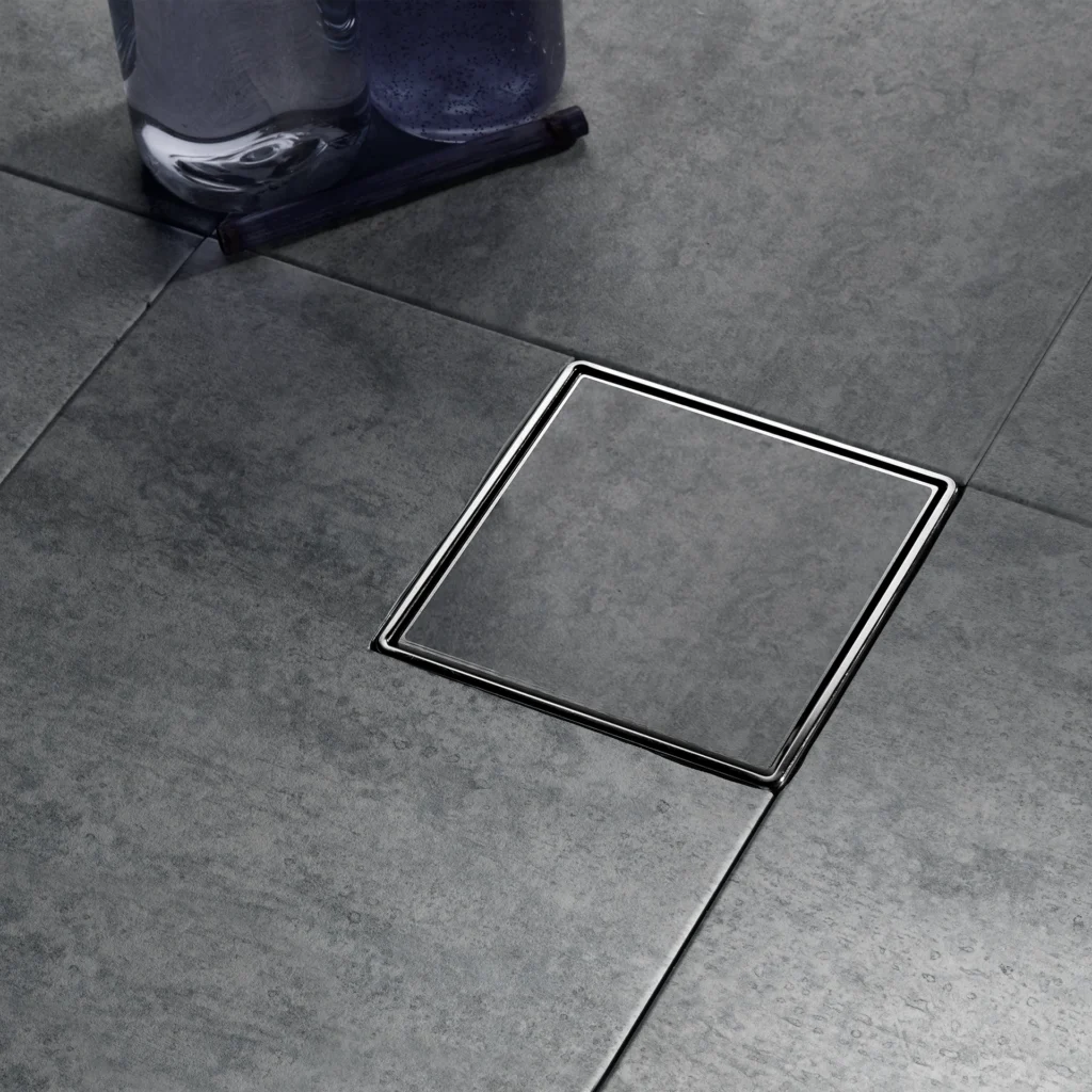 Dark blue bottle resting on gray tiled floor near a chrome floor drain