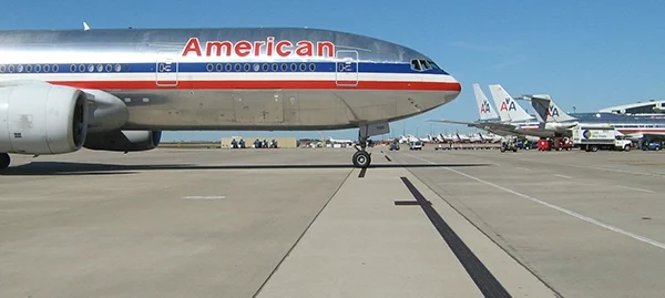 American Airlines jet on the tarmac with taxiway lines and several planes in the background, sunny day.