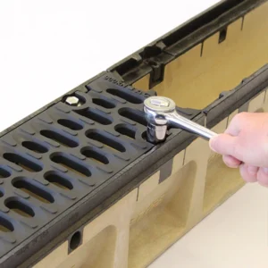 Hand using a socket wrench to tighten a bolt on a black plastic part with slots (likely a battery tray).