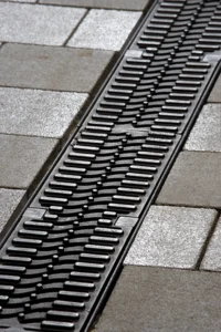 Close-up of a metal drainage grate embedded in a concrete sidewalk.
