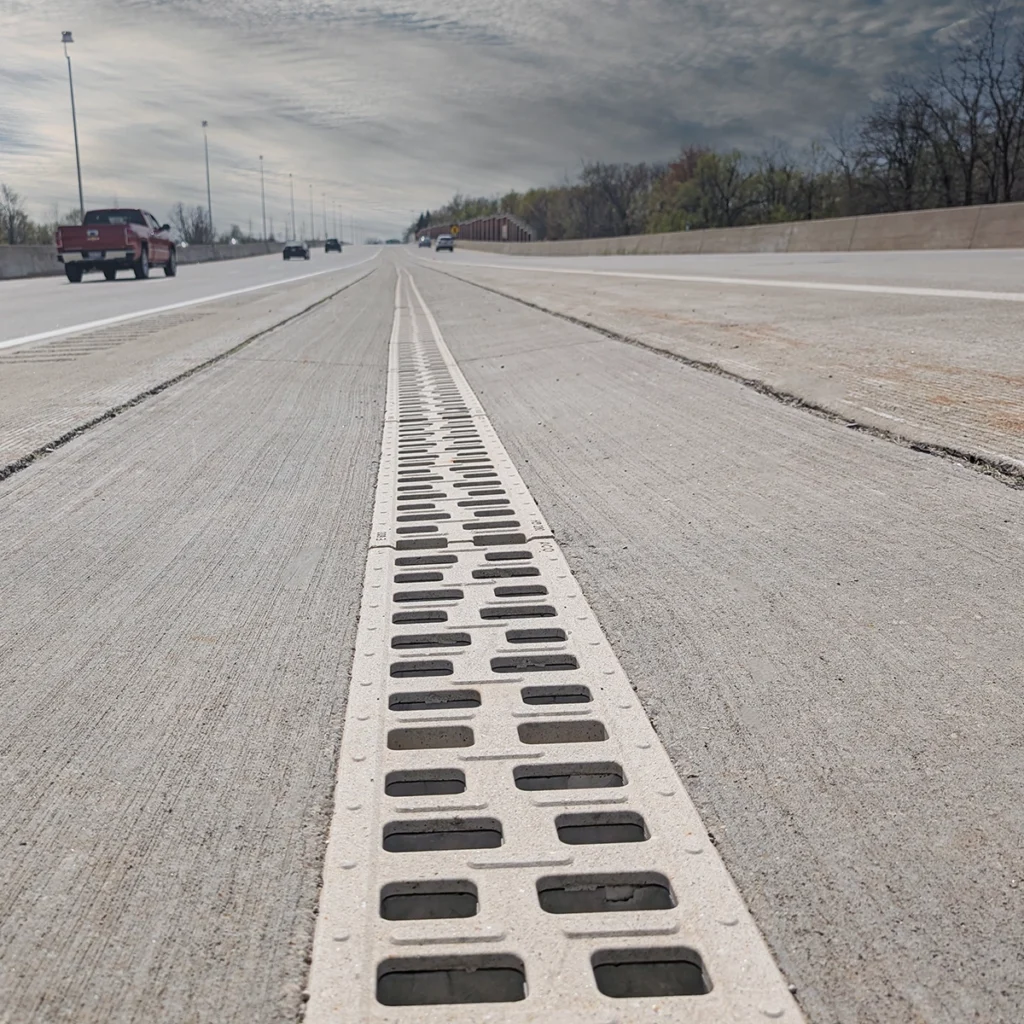 Low-angle view of a highway with a long perforated drainage grate running down the center toward the horizon.