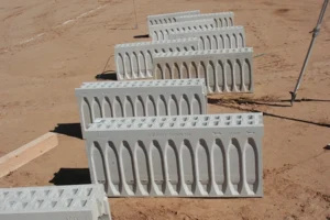 Row of precast concrete highway drainage blocks with vertical slots, laid in a dirt construction site for drainage